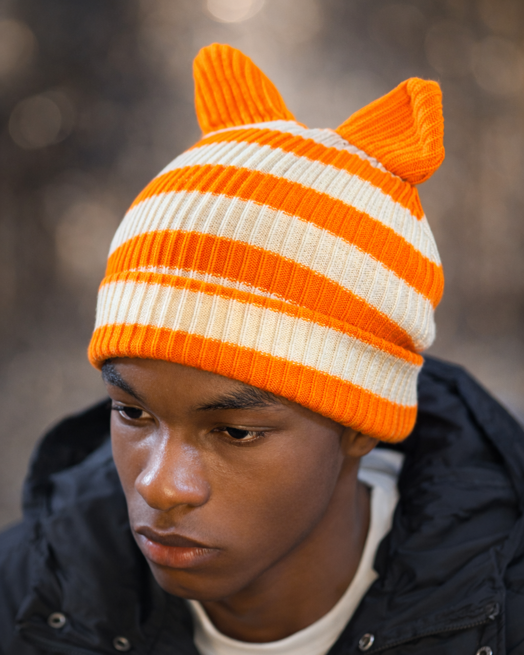 Person wearing an orange and white striped knit hat with cat ears against a blurred background