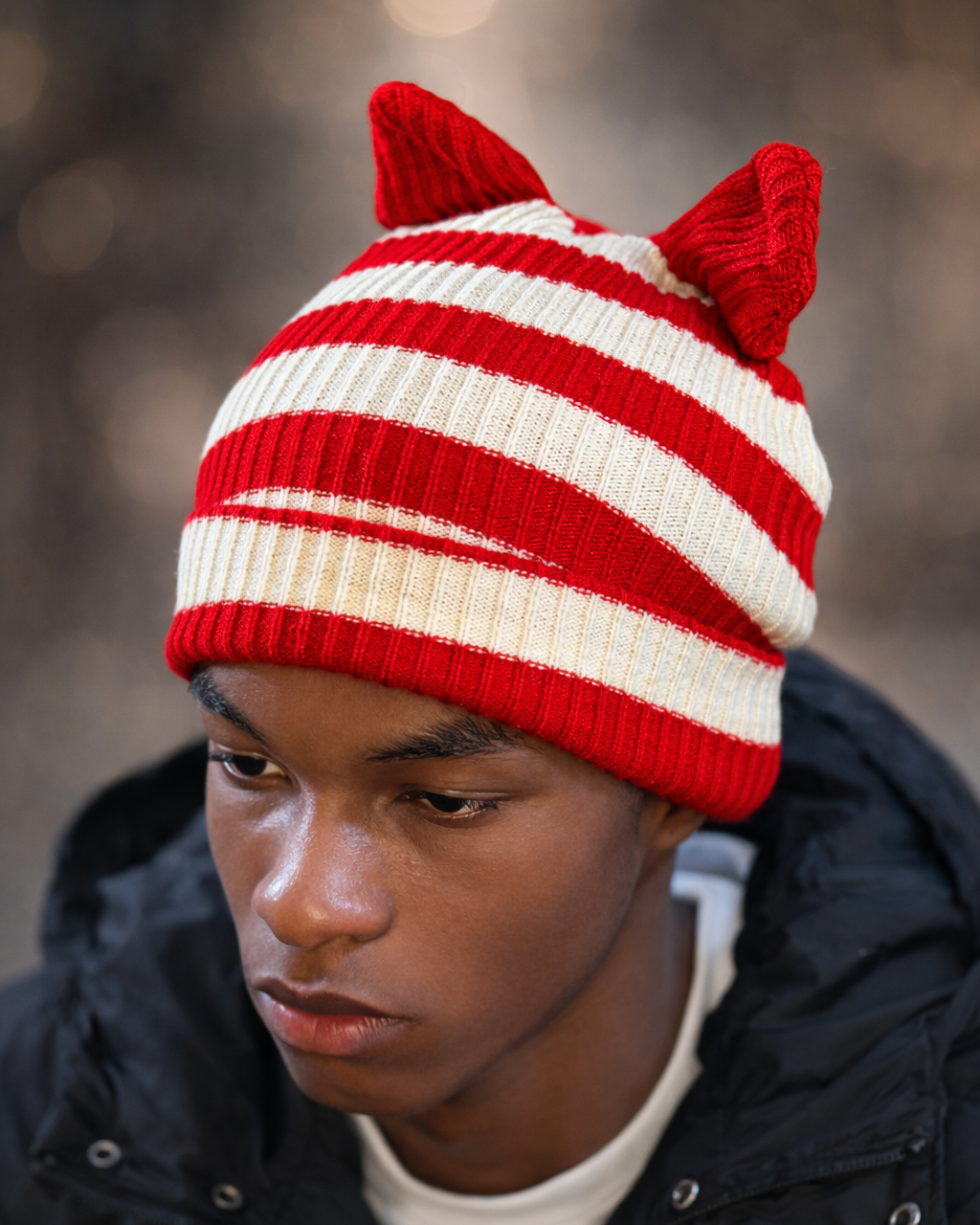 Person wearing a red and white striped knit hat with cat ears against a blurred background