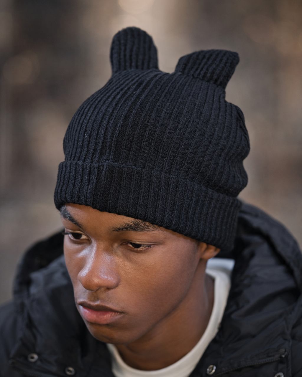 Person wearing a black knit beanie with bear ears against a blurred background